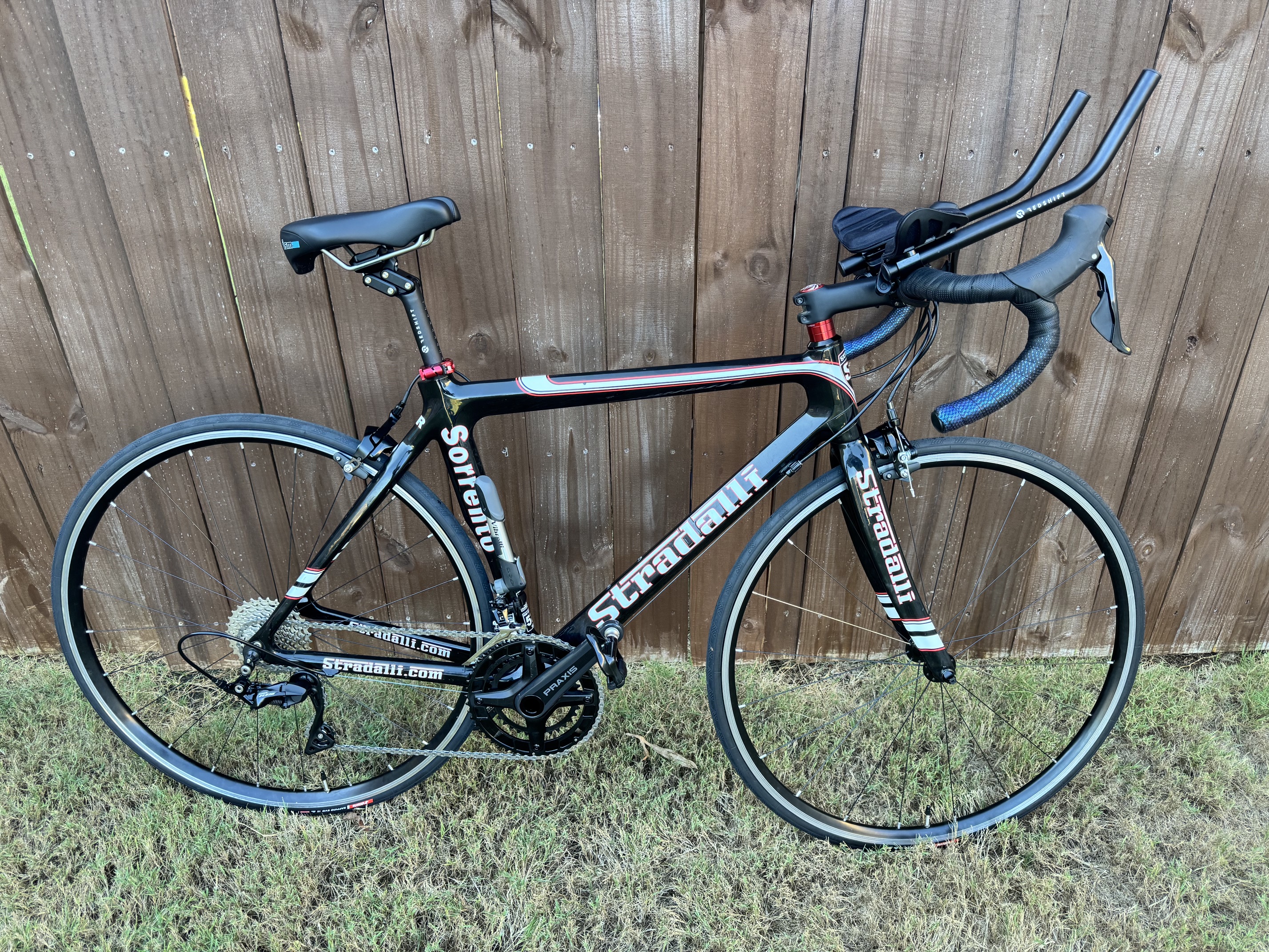 The fully assembled Stradalli Sorrento leaning against a wooden fence outdoors, with aerobars, wrapped drop bars, and a complete drivetrain.